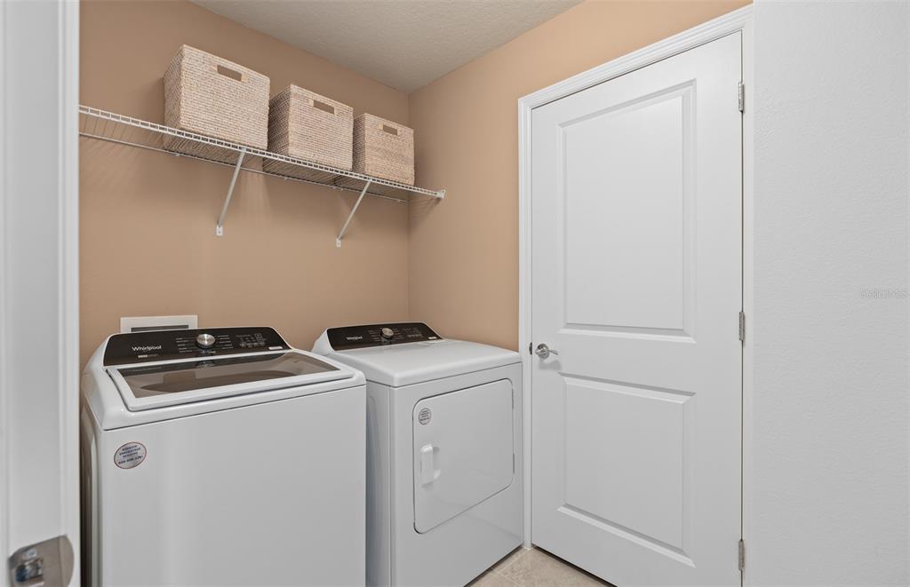 A laundry room features a white washer and dryer beneath a wire storage shelf — 6909 CREEK FALLS ALLEY, CLERMONT, FL