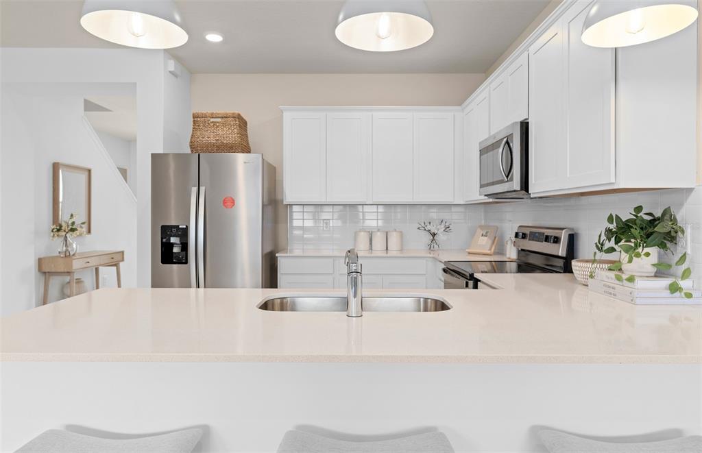 A kitchen features white cabinets, stainless steel appliances, and a quartz-topped island with a sink — 6909 CREEK FALLS ALLEY, CLERMONT, FL