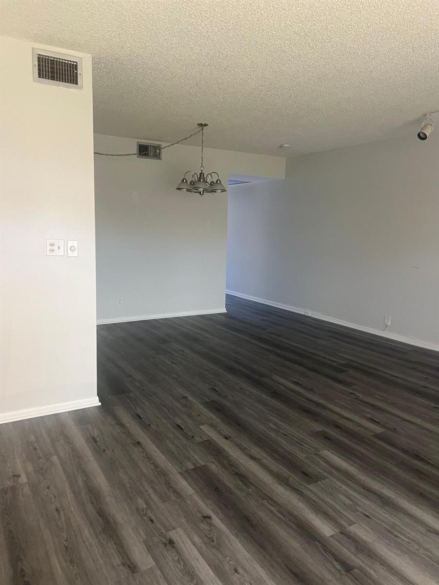 An empty room with gray wood-look flooring, white walls, and a hanging chandelier — 3402 Bimini Lane # E2, Coconut Creek FL 33066, COCONUT CREEK, FL