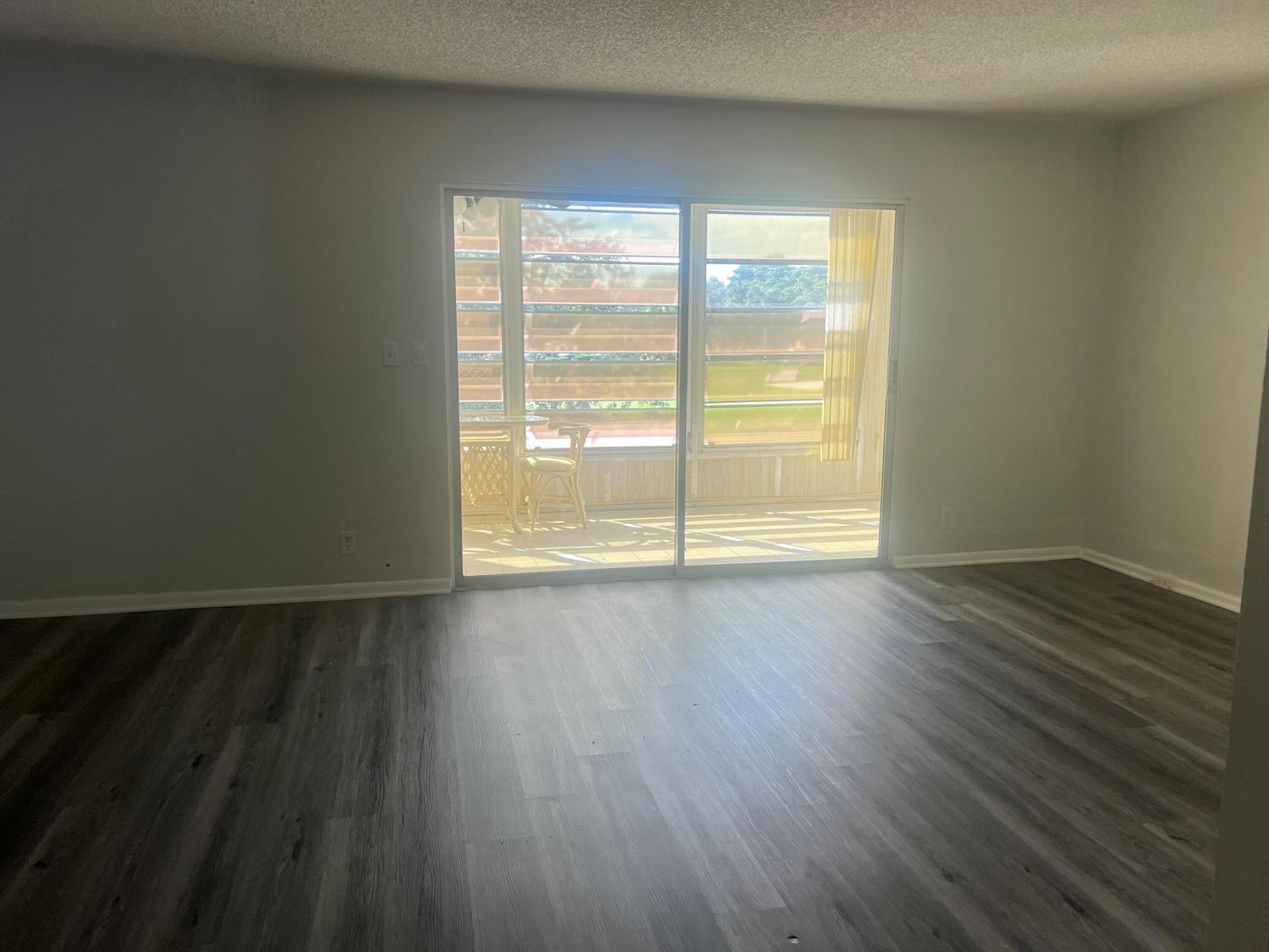 An empty room with gray wood-look flooring and a sliding glass door to a patio — 3402 Bimini Lane # E2, Coconut Creek FL 33066, COCONUT CREEK, FL