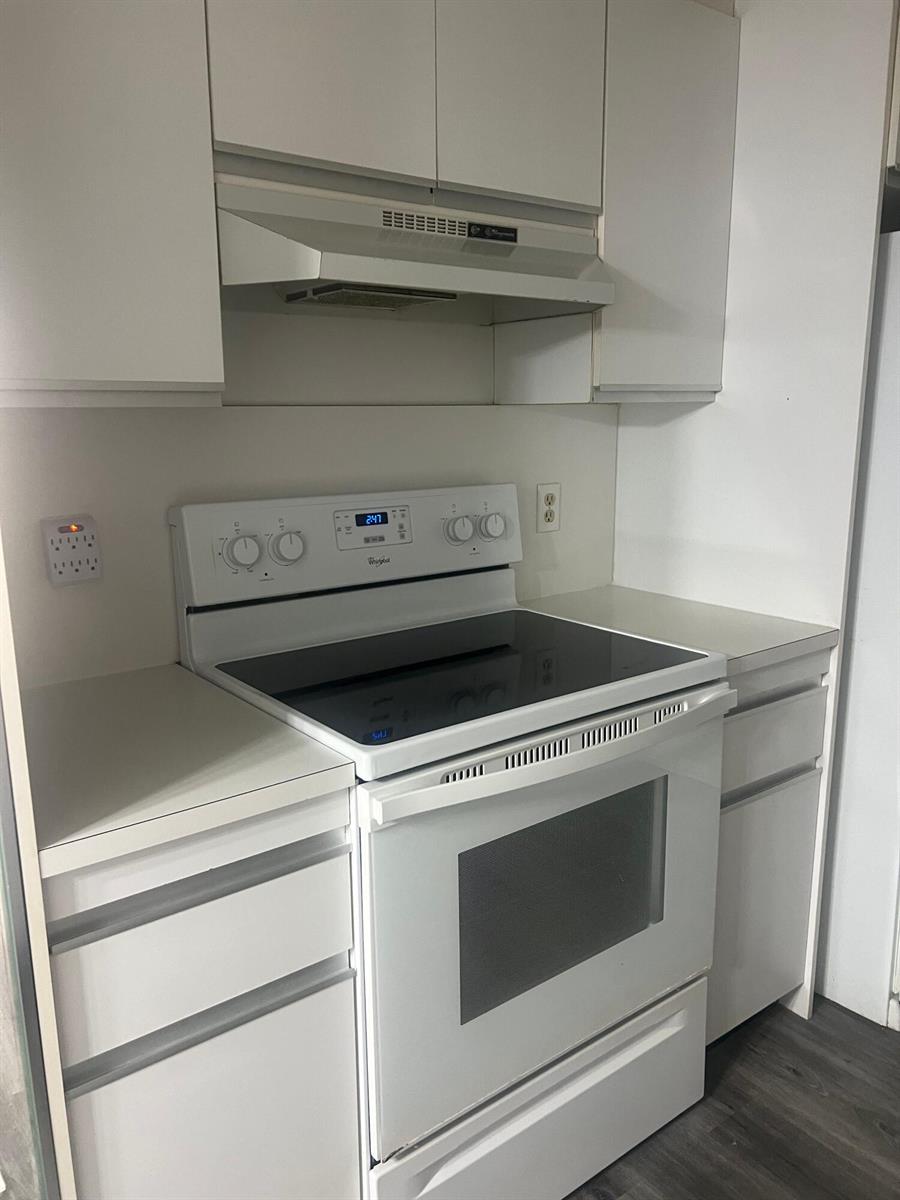 A white electric range and range hood are centered between white cabinets and countertops — 3402 Bimini Lane # E2, Coconut Creek FL 33066, COCONUT CREEK, FL