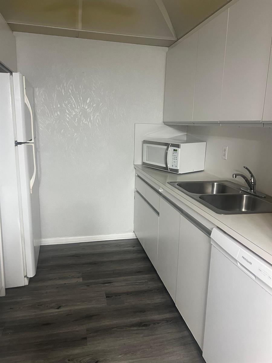 A galley kitchen features white cabinets, a double-basin sink, a microwave, and wood-look flooring — 3402 Bimini Lane # E2, Coconut Creek FL 33066, COCONUT CREEK, FL