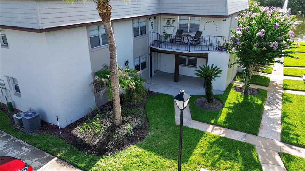 An exterior view of a two-story building with a balcony, patio, and landscaped lawn — 53 WINDTREE LANE UNIT 102, WINTER GARDEN, FL