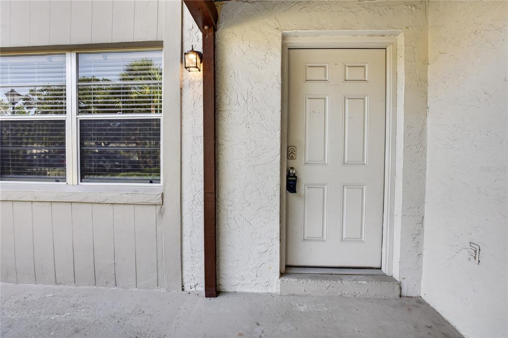A white front door with a digital lock sits next to a window on a patio — 53 WINDTREE LANE UNIT 102, WINTER GARDEN, FL
