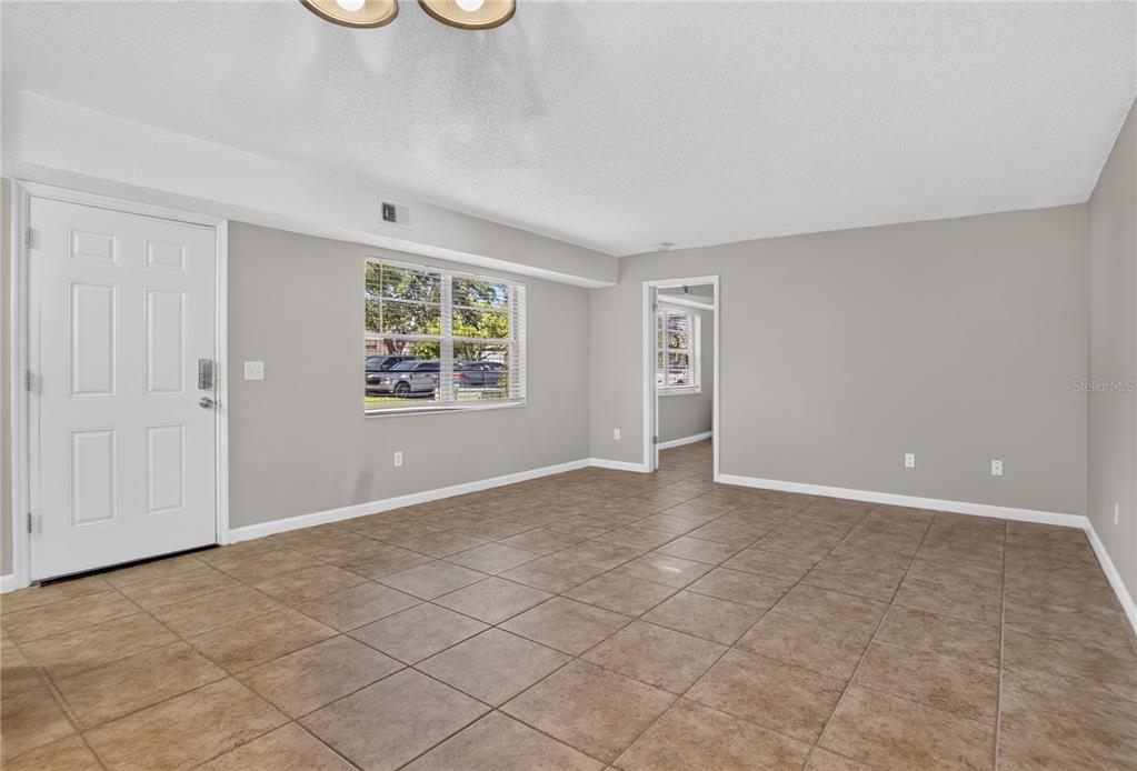 An empty room with light gray walls, brown tile flooring, and a white entry door — 53 WINDTREE LANE UNIT 102, WINTER GARDEN, FL