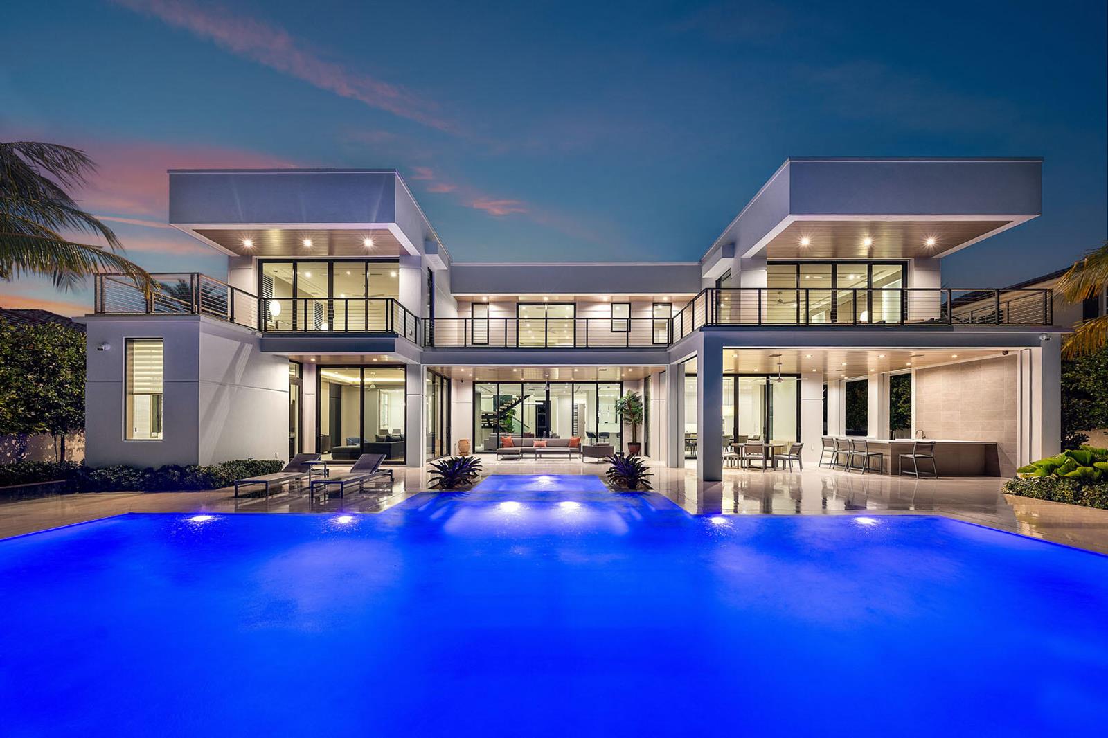 A modern two-story house with a large illuminated swimming pool and patio at dusk — 175 W Alexander Palm Road, Boca Raton FL 33432, BOCA RATON, FL