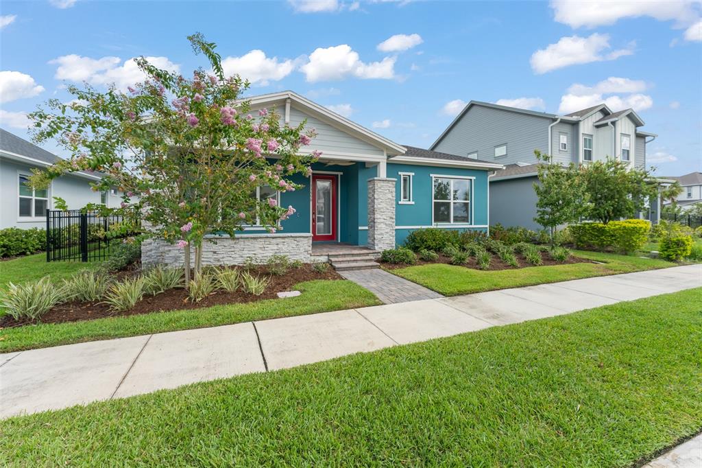 A teal single-story house with a stone facade, red front door, and a landscaped yard — 13550 MCMILLAN DRIVE, ORLANDO, FL