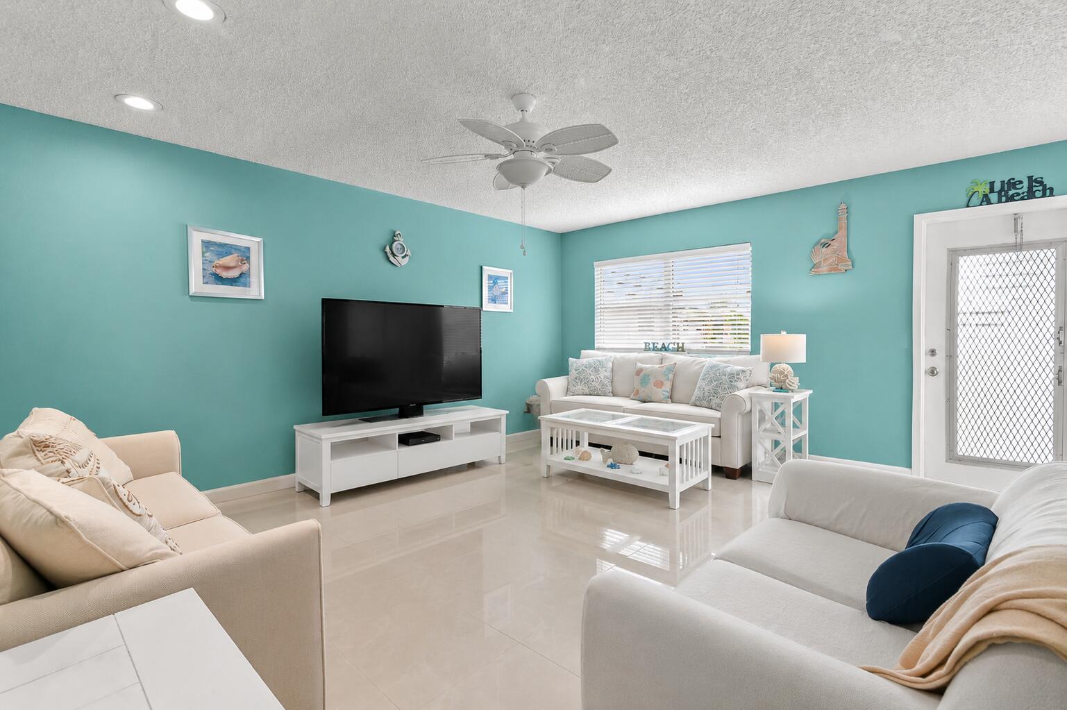 A living room features light blue walls, white furniture, a ceiling fan, and tile flooring — 520 Monaco K, Delray Beach FL 33446, DELRAY BEACH, FL