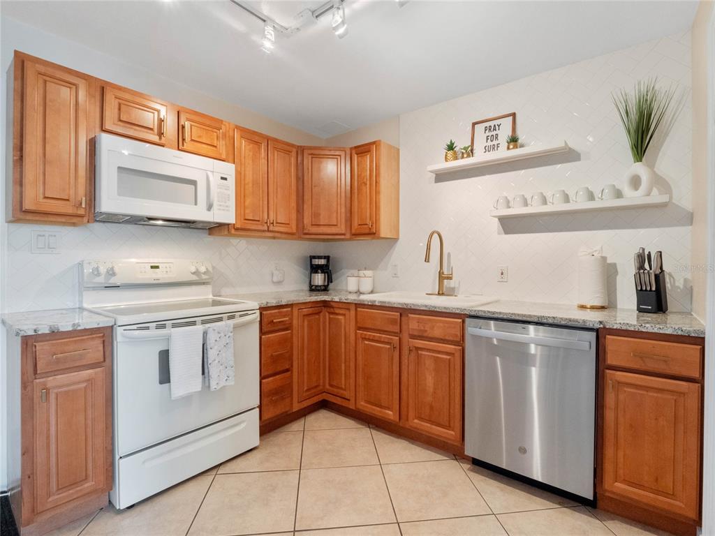 A kitchen with wood cabinets, white appliances, granite countertops, and a white tile backsplash — 218 CANAVERAL BEACH BOULEVARD, CAPE CANAVERAL, FL