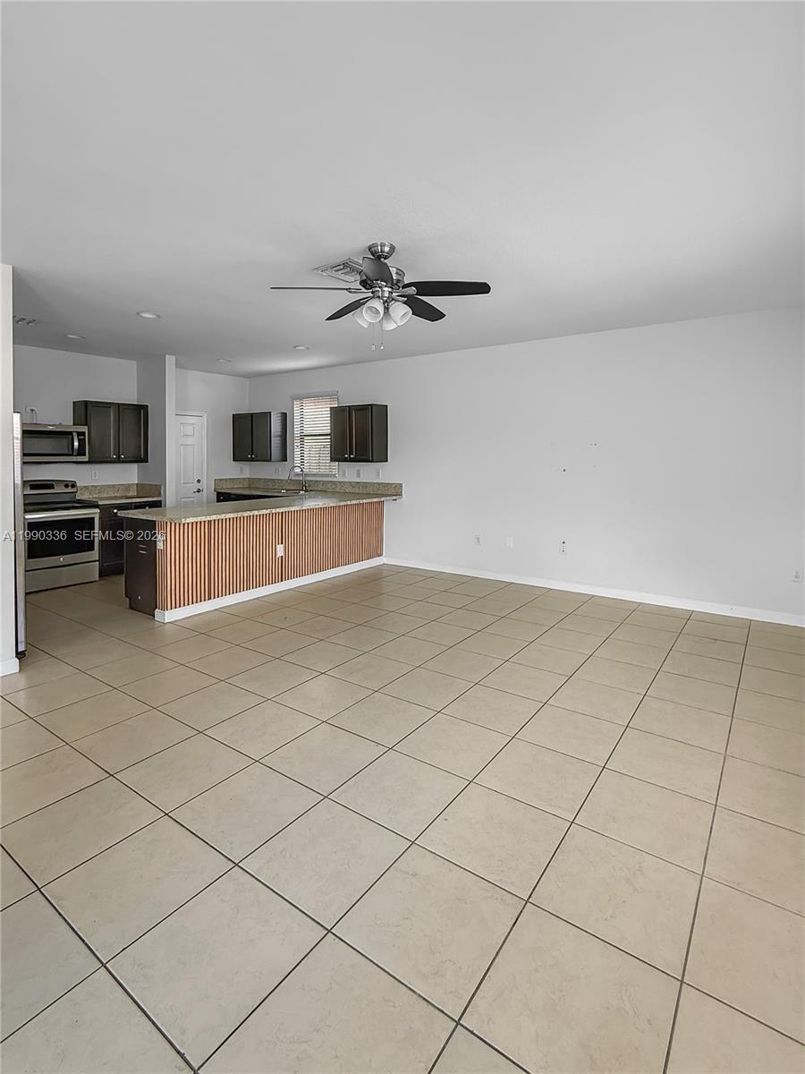 An open-concept kitchen features dark cabinetry, a slatted breakfast bar, and light tile flooring — 709 SE 35th Ave, Homestead FL 33033, HOMESTEAD, FL