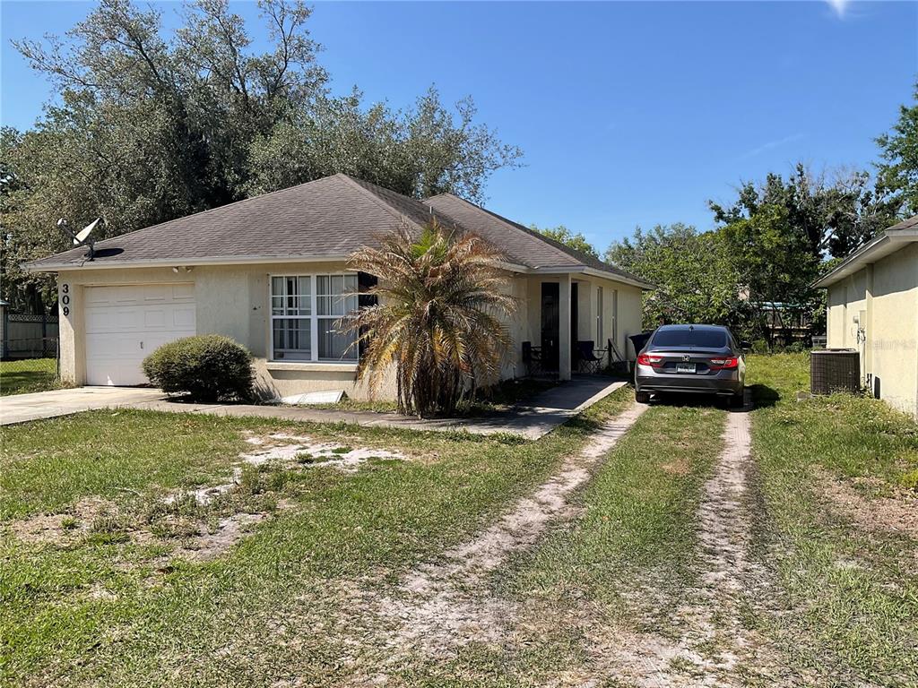 A single-story house with a white garage, a palm tree, and a car in the driveway — 309 NW 9TH STREET, MULBERRY, FL