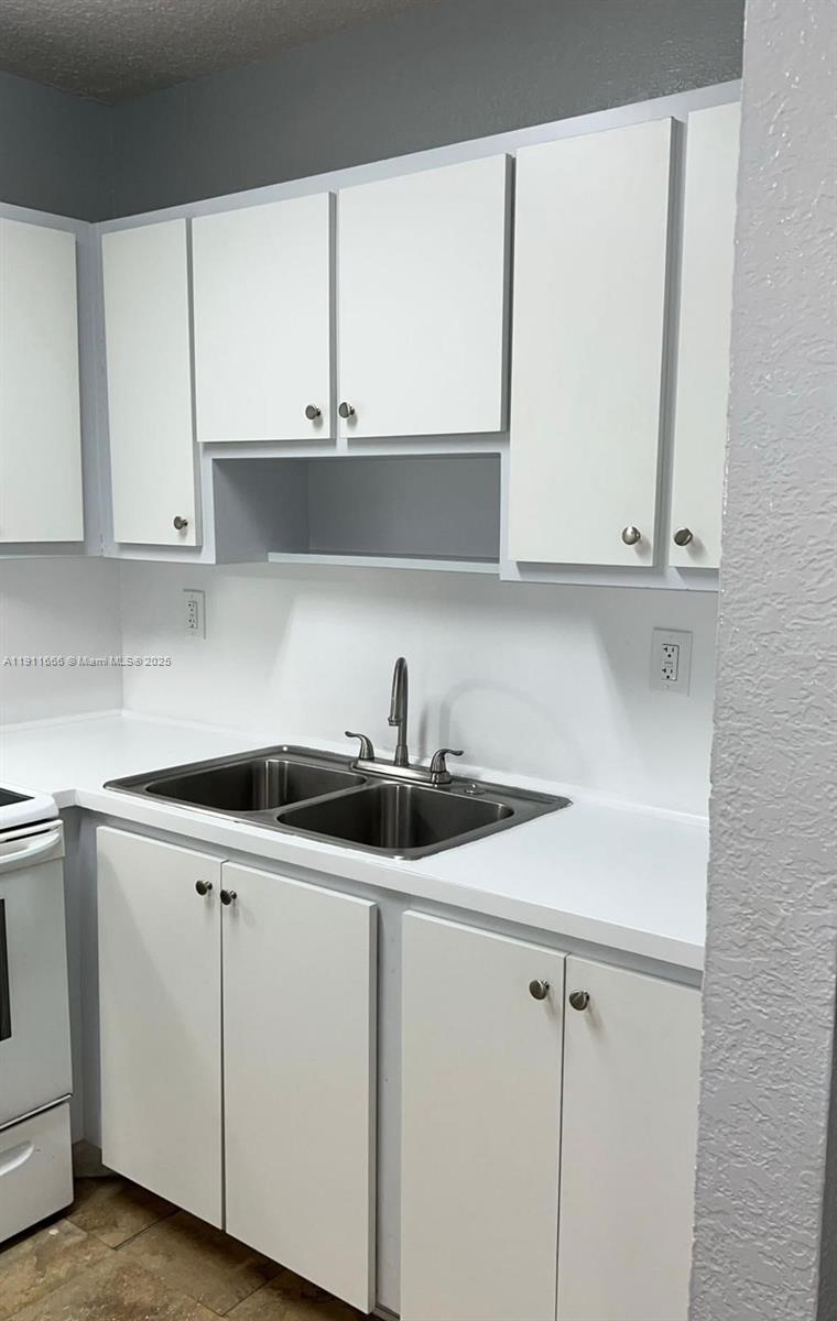 This kitchen features white cabinets, a double-basin stainless steel sink, and white countertops — 575 W 69th St # 208, Hialeah FL 33014, HIALEAH, FL