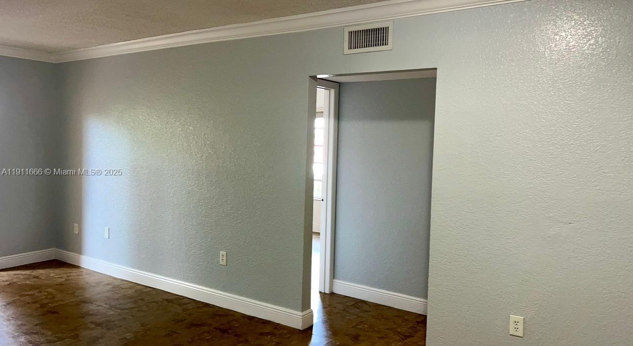 A room with light blue walls, crown molding, and dark wood-look flooring features a doorway — 575 W 69th St # 208, Hialeah FL 33014, HIALEAH, FL