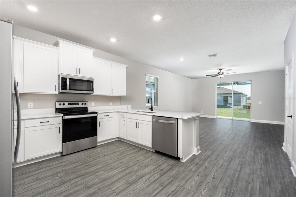 A modern kitchen with white cabinets, stainless steel appliances, and gray wood-look flooring — 3343 CHINOTTO DRIVE, LAKE ALFRED, FL