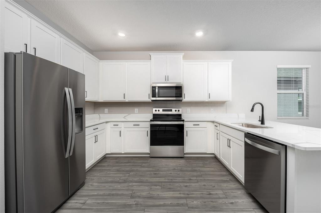 A modern kitchen features white cabinets, stainless steel appliances, and gray wood-look flooring — 3343 CHINOTTO DRIVE, LAKE ALFRED, FL