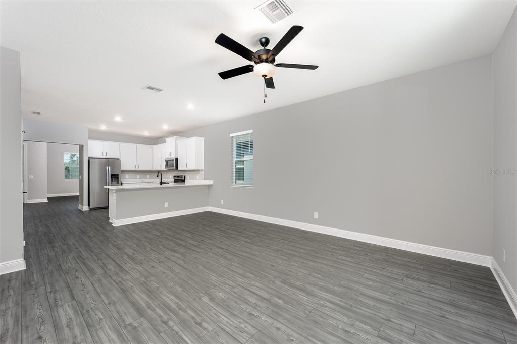 An open-concept living area features gray wood-look flooring, white kitchen cabinets, and a ceiling fan — 3343 CHINOTTO DRIVE, LAKE ALFRED, FL