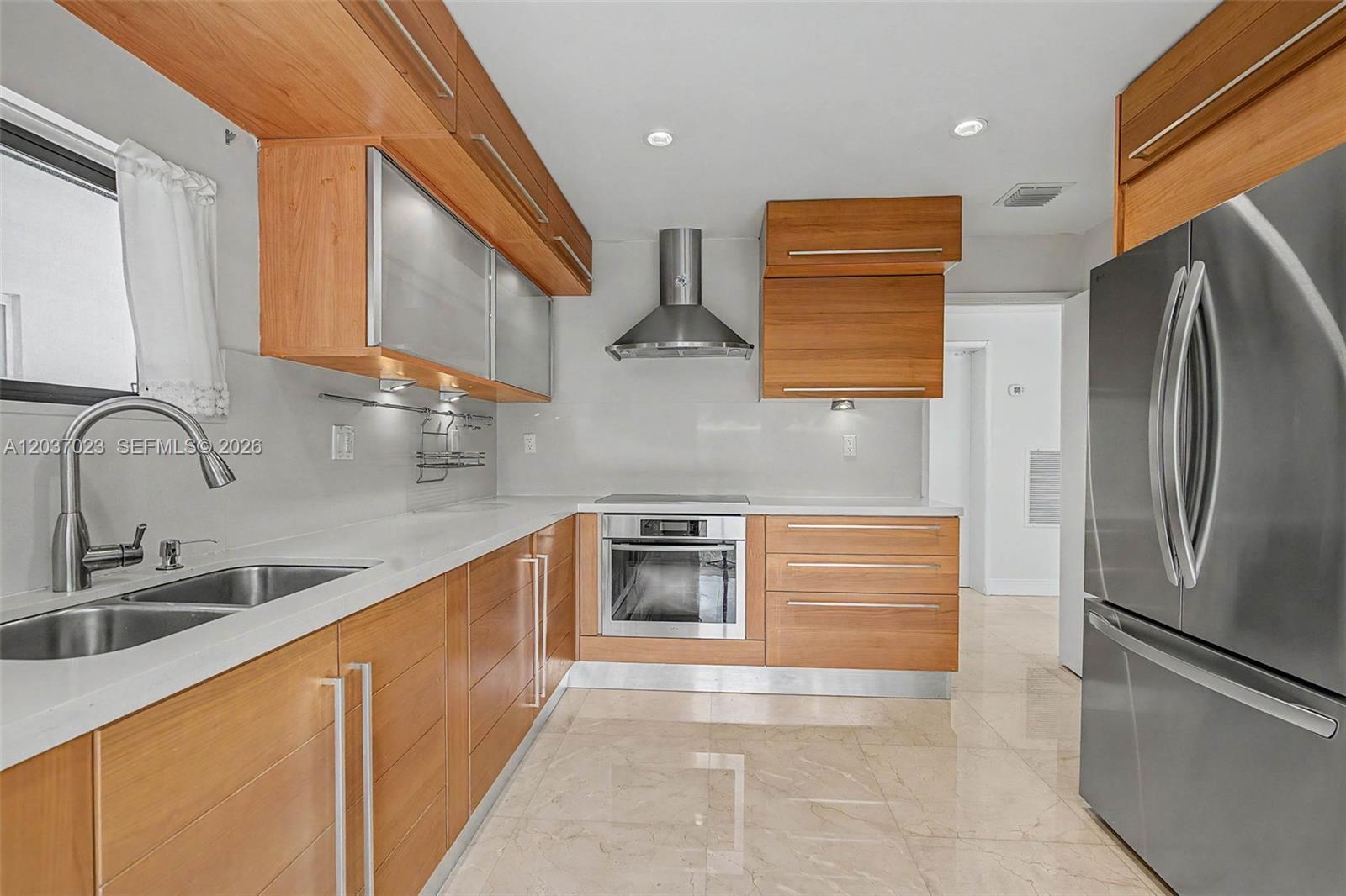 A modern kitchen features wood cabinets, stainless steel appliances, and light-colored countertops and flooring — 4950 San Amaro Dr, Coral Gables FL 33146, CORAL GABLES, FL