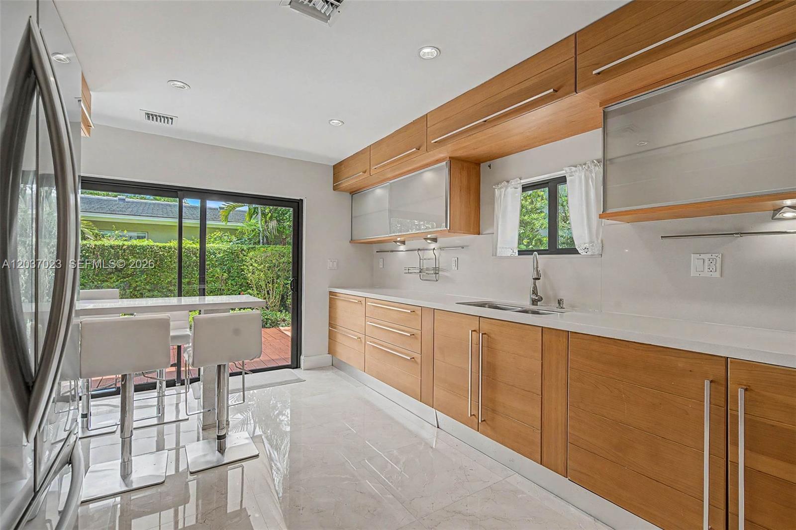 A modern kitchen features light wood cabinetry, white countertops, stainless steel appliances, and tile flooring — 4950 San Amaro Dr, Coral Gables FL 33146, CORAL GABLES, FL
