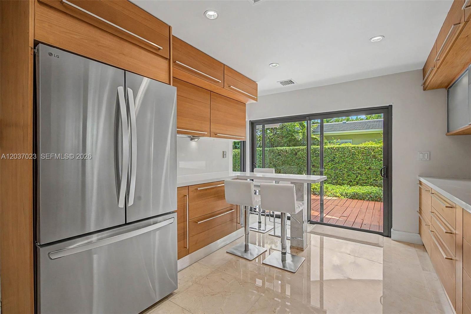 A modern kitchen features wood cabinetry, stainless steel appliances, a breakfast bar, and sliding doors — 4950 San Amaro Dr, Coral Gables FL 33146, CORAL GABLES, FL