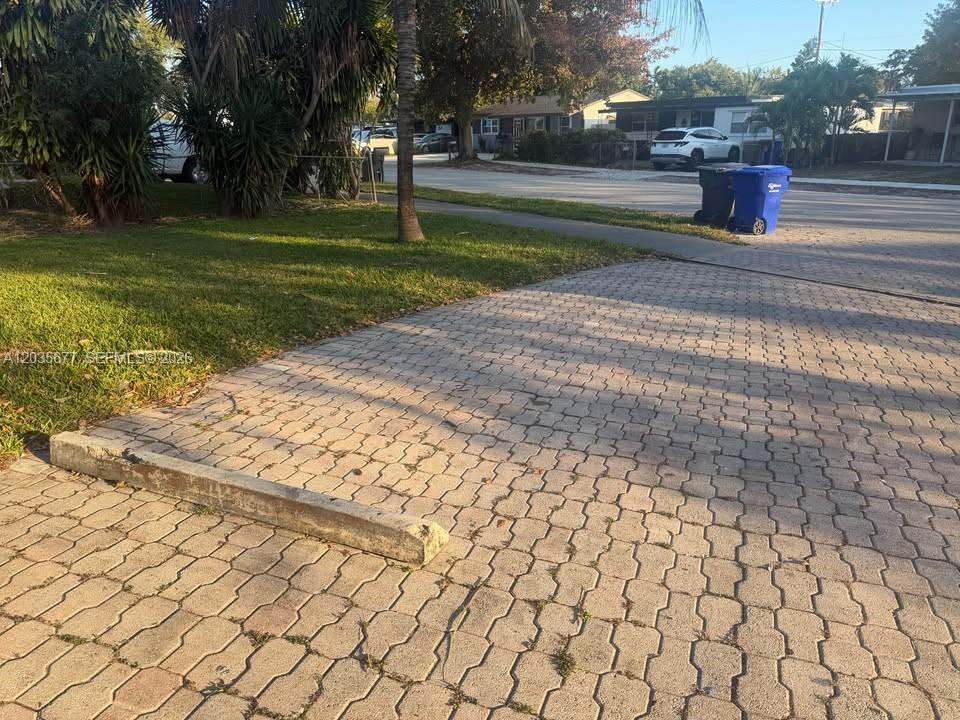 A paved driveway features a concrete parking stop next to a grassy lawn and street — HOLLYWOOD, FL