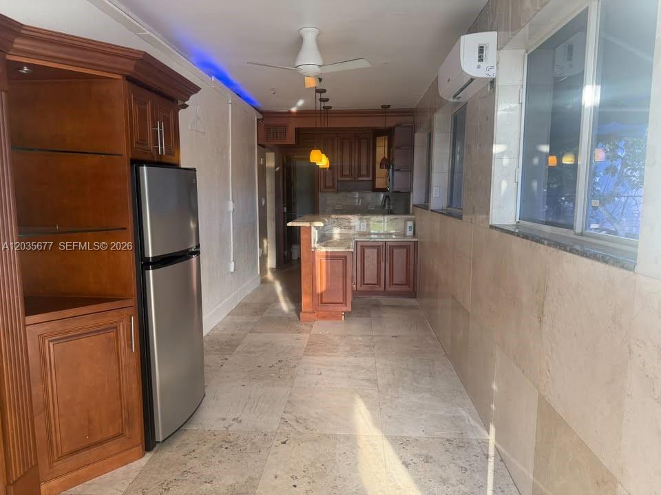 A kitchen features wood cabinets, a stainless steel refrigerator, and light-colored stone floor tiles — HOLLYWOOD, FL