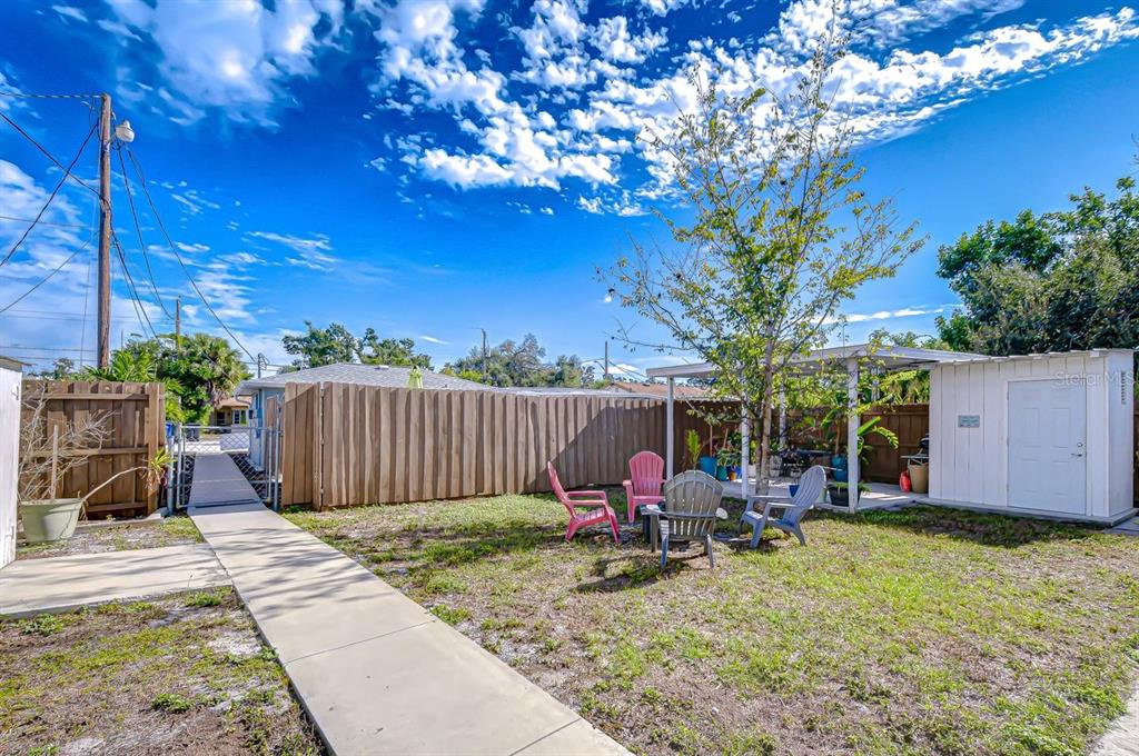 A backyard features a concrete walkway, a wooden fence, a shed, and several outdoor chairs — 4444 17TH STREET W UNIT B, BRADENTON, FL