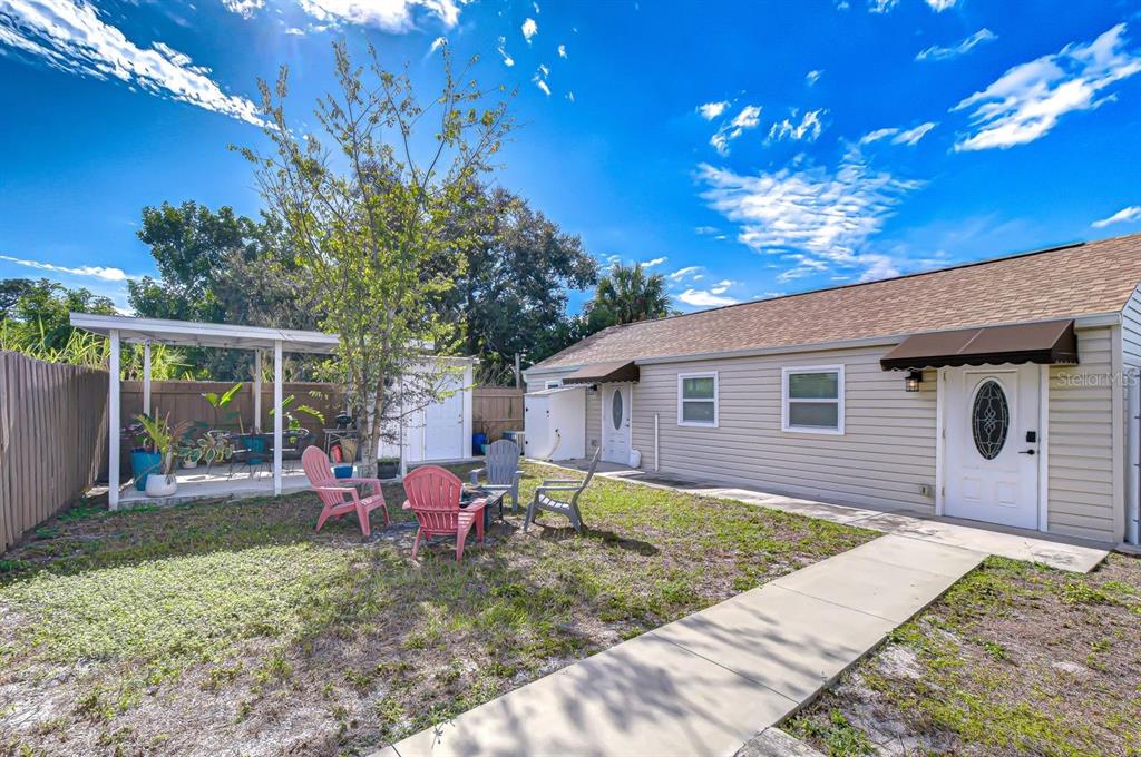 A backyard with a concrete walkway, a small patio cover, and several outdoor chairs — 4444 17TH STREET W UNIT B, BRADENTON, FL