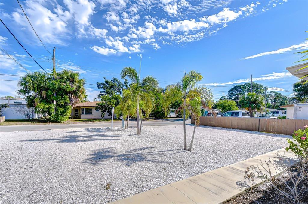 A gravel yard features several palm trees and a wooden fence under a blue sky — 4444 17TH STREET W UNIT B, BRADENTON, FL