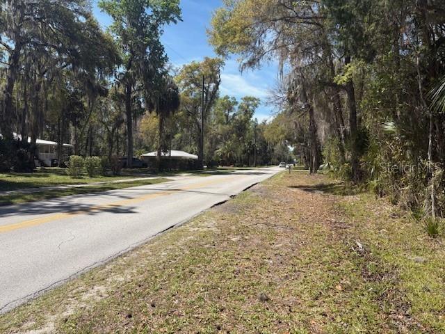 A paved road stretches through a wooded residential area with houses visible in the distance — 1325 NW 19TH STREET, CRYSTAL RIVER, FL