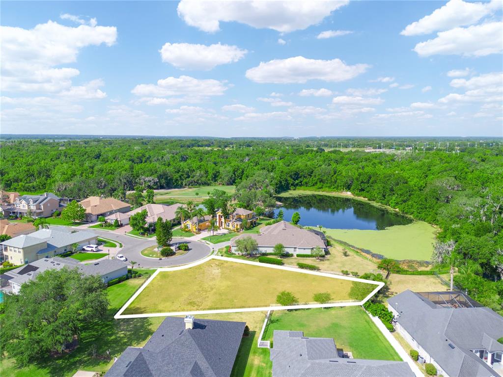An aerial view shows a vacant, trapezoidal residential lot situated near a pond and houses — WHISPER WOODS DRIVE, LAKELAND, FL