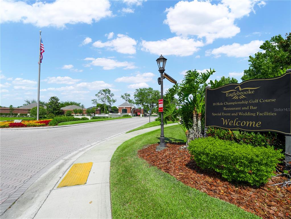 A sign for Eaglebrooke Golf Course stands beside a paved entrance road under a blue sky — WHISPER WOODS DRIVE, LAKELAND, FL
