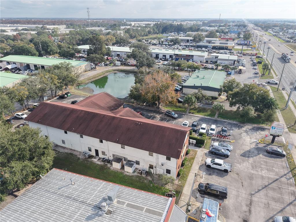 An aerial view shows a multi-story building with a brown roof next to a pond — 9753 S ORANGE BLOSSOM TRAIL UNIT 103, ORLANDO, FL