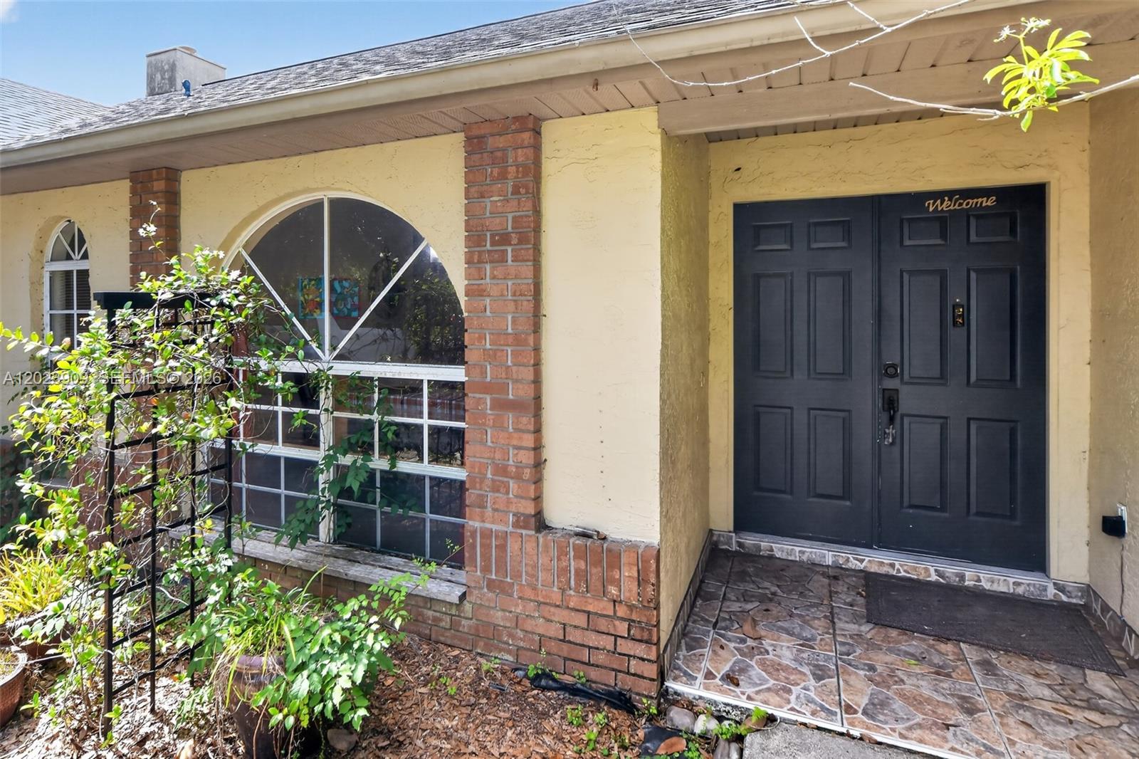 The exterior of a house features a brick-accented wall, a large arched window, and double doors — 10300 YORKMERE CT, Orlando FL 32817, ORLANDO, FL