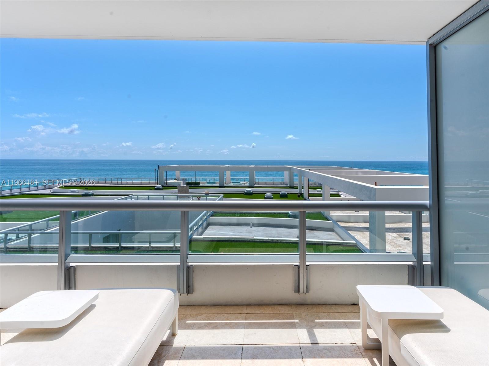 A balcony with white lounge chairs overlooks a modern building terrace and the ocean — 6799 Collins Ave # 704, Miami Beach FL 33141, MIAMI BEACH, FL