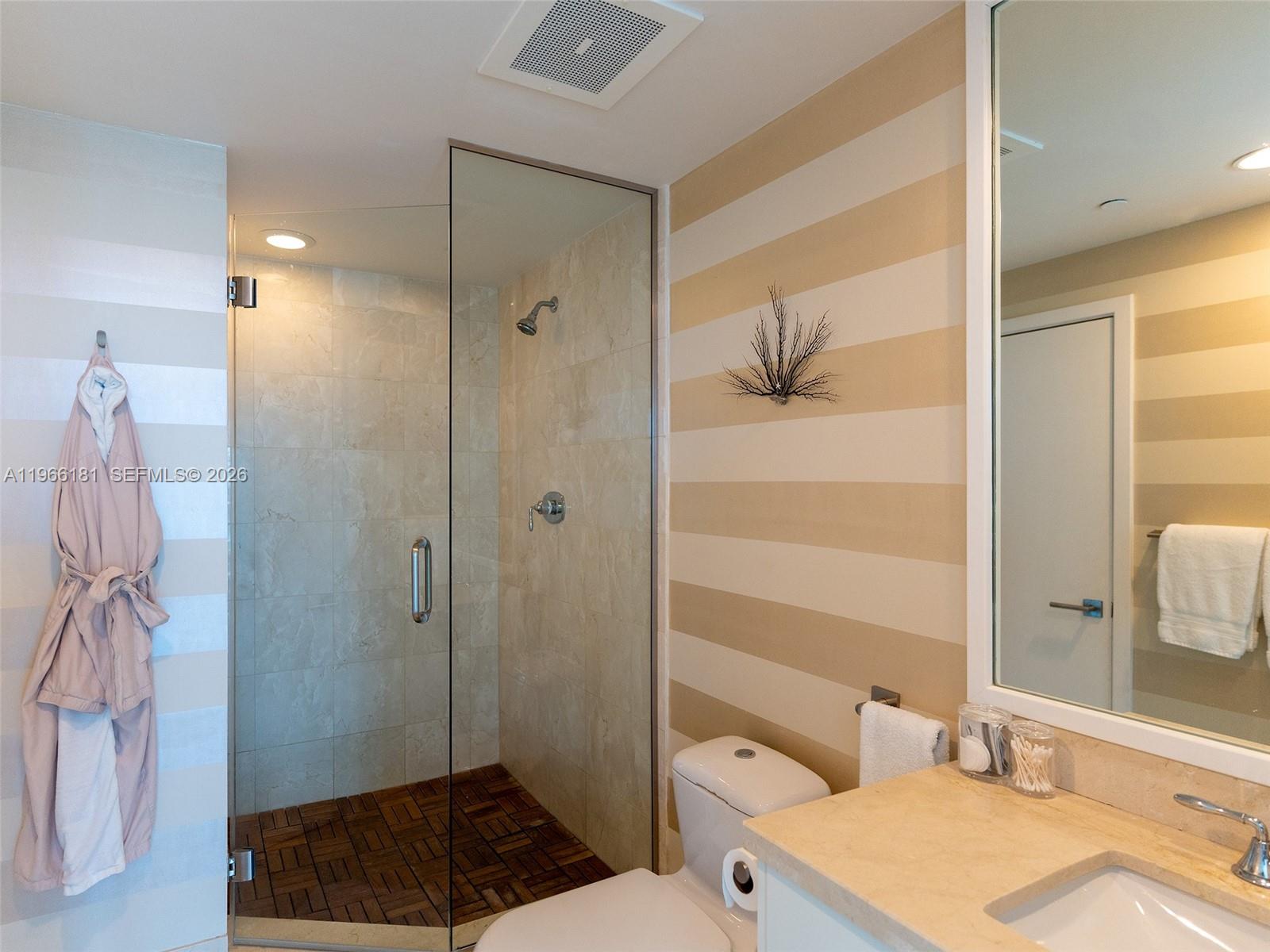 A bathroom features a glass-enclosed shower with wood flooring, beige striped walls, and a vanity — 6799 Collins Ave # 704, Miami Beach FL 33141, MIAMI BEACH, FL