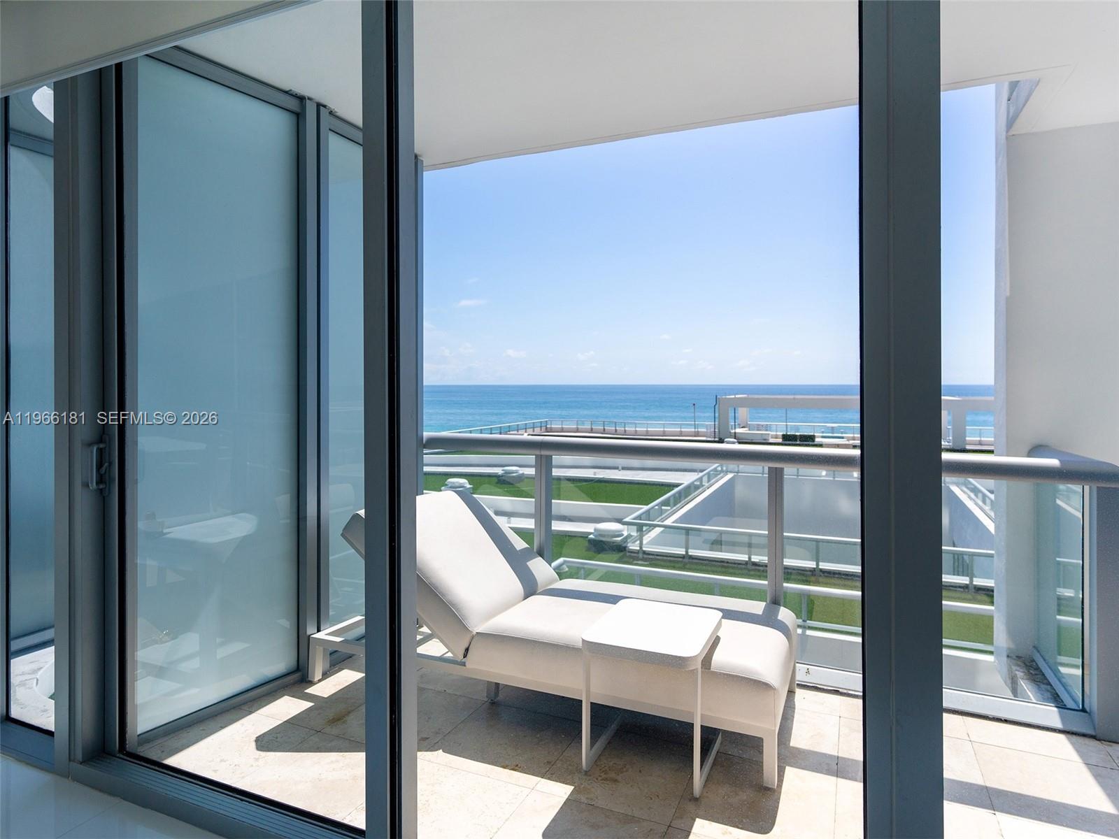 A white lounge chair sits on a balcony overlooking the ocean and a pool deck — 6799 Collins Ave # 704, Miami Beach FL 33141, MIAMI BEACH, FL