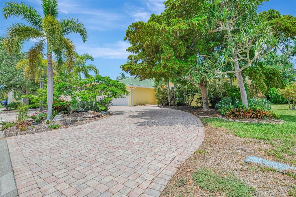 A paved driveway leads to a yellow house surrounded by lush trees and palm trees — 4708 SWEETMEADOW CIRCLE, SARASOTA, FL