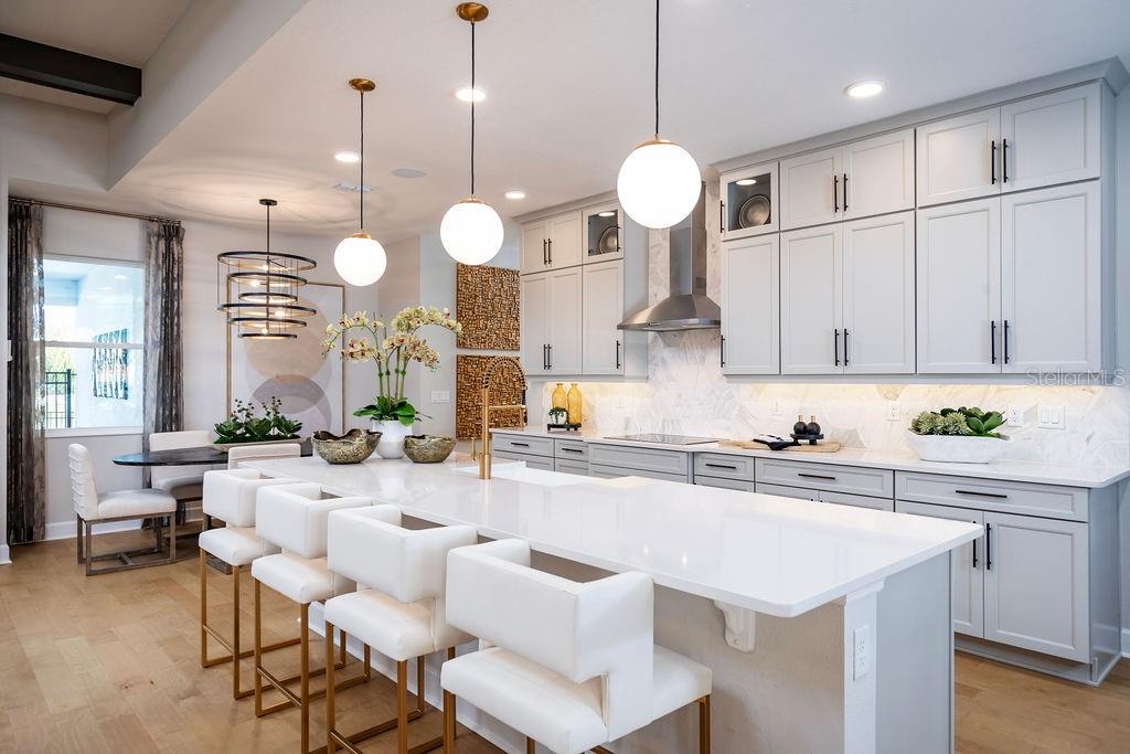 A modern kitchen features white cabinets, a large quartz island, and gold-accented bar stools — 2739 RAVENCLIFFE TERRACE, OVIEDO, FL