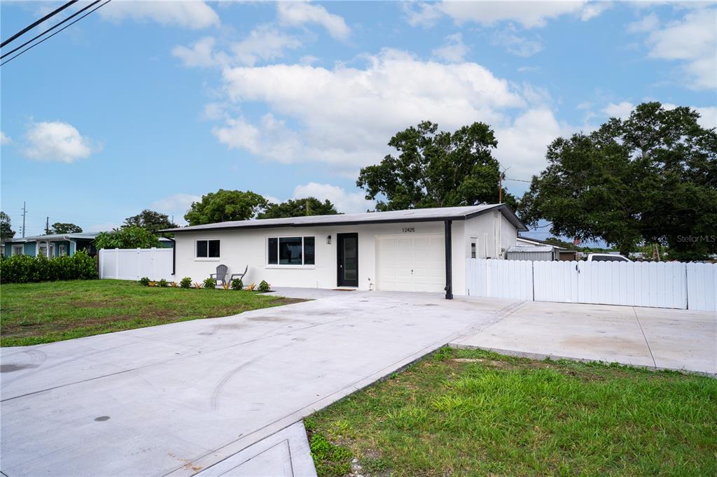 A white single-story house features a concrete driveway, a garage, and a white vinyl fence — 12425 RIDGE ROAD, LARGO, FL