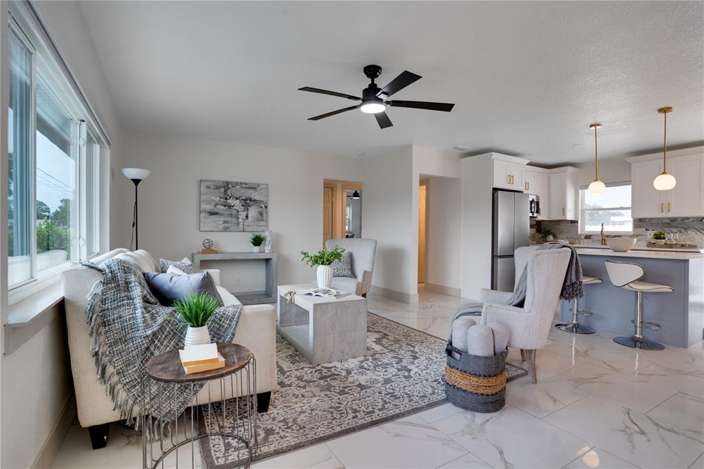 An open-concept living room and kitchen featuring white cabinetry, marble-look tile floors, and neutral furniture — 12425 RIDGE ROAD, LARGO, FL