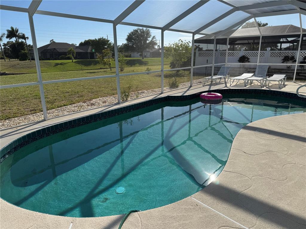 A swimming pool with a pink float sits inside a screened-in lanai overlooking a yard — 640 BOUNDARY BOULEVARD, ROTONDA WEST, FL