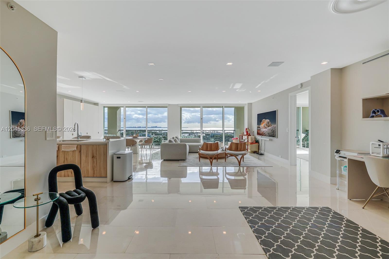 A bright, open-concept living area features a modern kitchen, dining space, and balcony with water views — 3400 SW 27th Ave # 802, Miami FL 33133, MIAMI, FL
