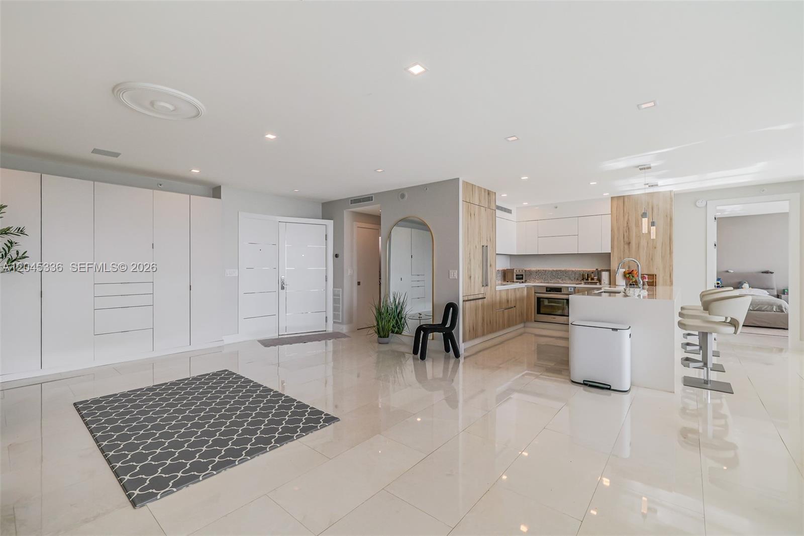 A modern open-concept kitchen and living area features white cabinetry, light wood accents, and tile flooring — 3400 SW 27th Ave # 802, Miami FL 33133, MIAMI, FL