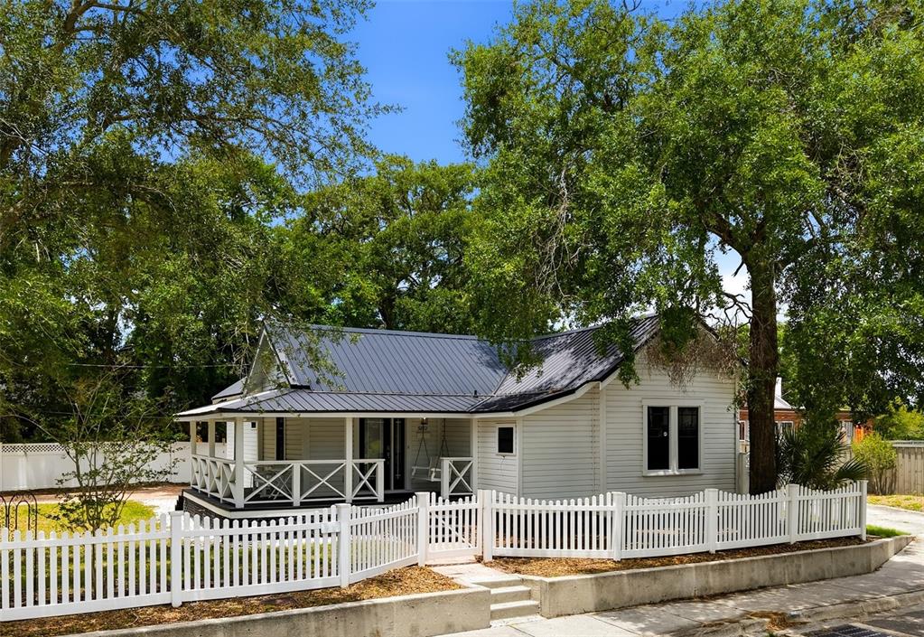 A white cottage with a metal roof and a wrap-around porch behind a picket fence — 5602 N OLA AVENUE, TAMPA, FL