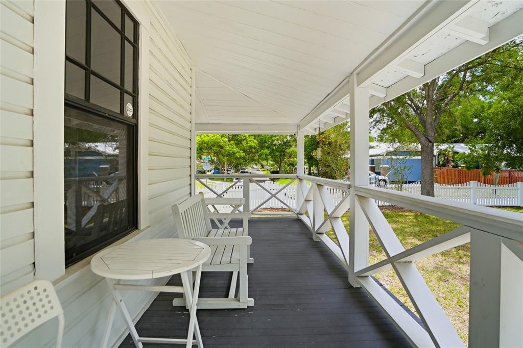 A covered wooden porch features white railings, a small round table, and a bench — 5602 N OLA AVENUE, TAMPA, FL
