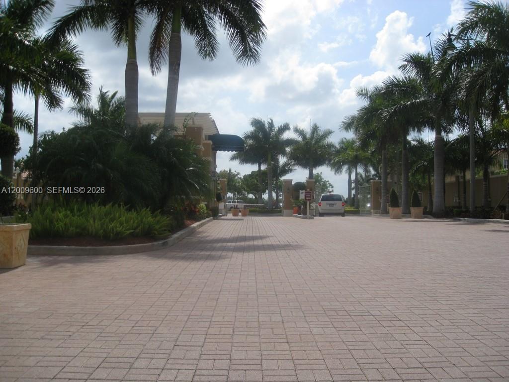 A paved driveway leads to the gated entrance of a residential community with palm trees — 6630 NW 114th AV # 1503, Doral FL 33178, DORAL, FL