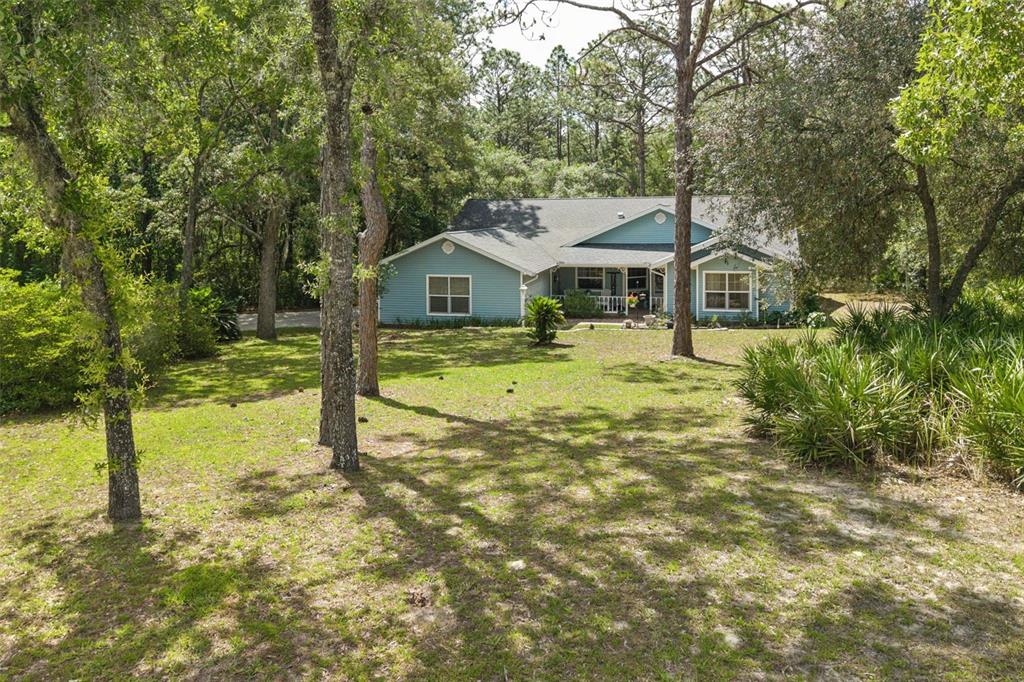 A blue single-story house sits in a grassy, wooded yard with mature trees — 4381 N CAPISTRANO LOOP, BEVERLY HILLS, FL
