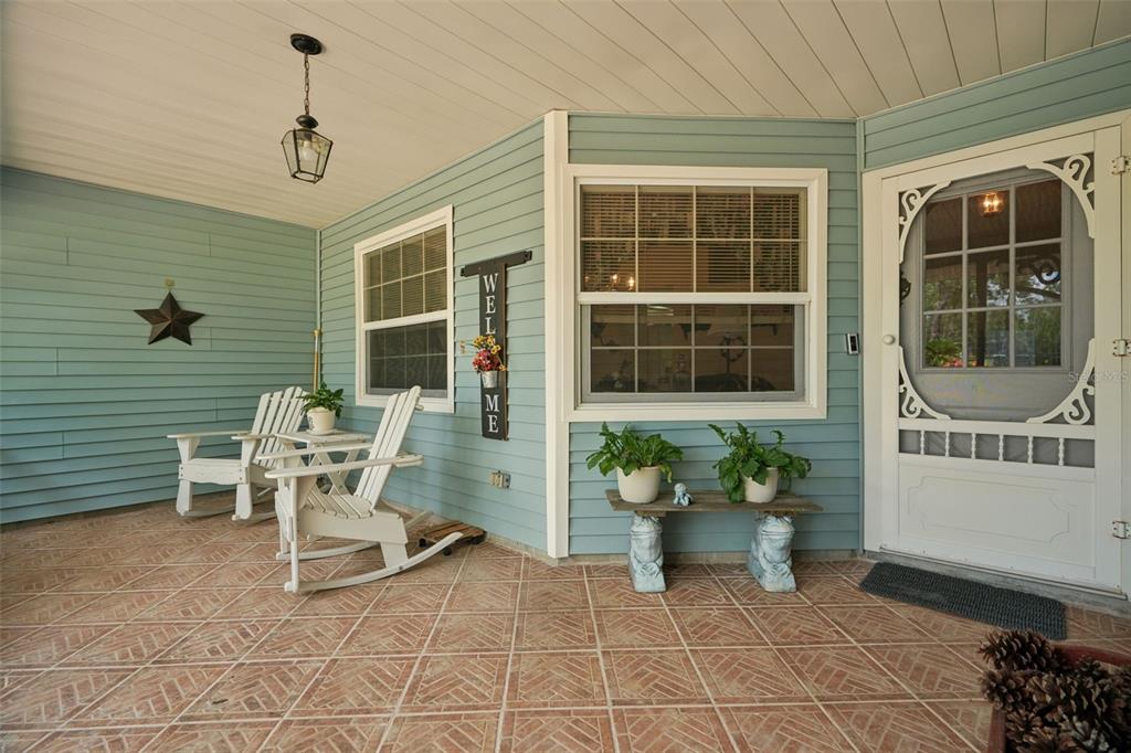 A covered front porch features light blue siding, tiled flooring, rocking chairs, and a screen door — 4381 N CAPISTRANO LOOP, BEVERLY HILLS, FL