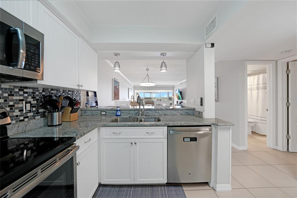 A kitchen with white cabinets, granite countertops, stainless steel appliances, and a pass-through window — 1701 BEACH ROAD UNIT 202, ENGLEWOOD, FL