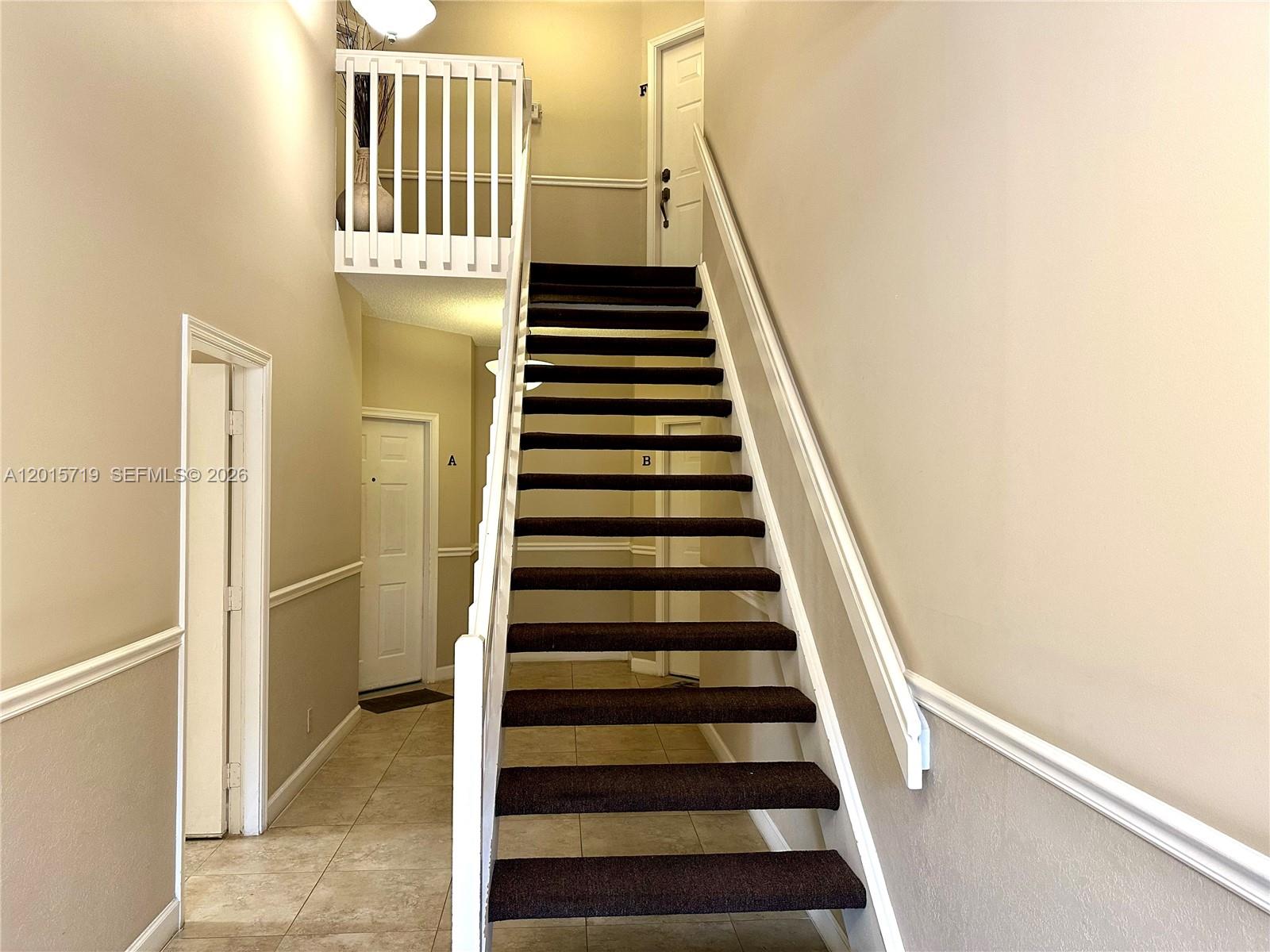 A carpeted staircase with white railings leads to an upper landing in a neutral-toned foyer — 5790 Coach House Cir, Boca Raton FL 33486, BOCA RATON, FL